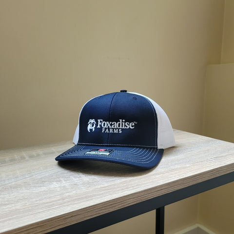 Navy and white cap with 'Foxadise Farms' logo on a wooden surface.