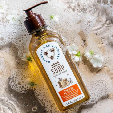 A clear pump bottle of Tupelo Honey Hand Soap with a yellow label, placed on a surface with bubbles and floral patterns.