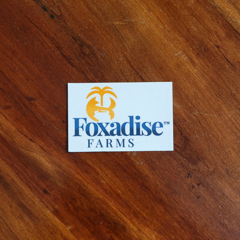 A round vinyl sticker with a blue and white design featuring a palm tree and what appears to be a fox face, placed on a wooden surface.
