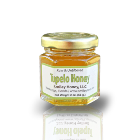 A jar of Tupelo Honey with a label indicating it is raw and unfiltered, produced by Smiley Honey, LLC, with a net weight of 2 oz (56 g).