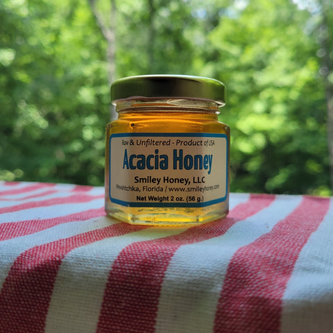 Jar of Acacia honey from Smiley Honey, LLC on a striped fabric with a blurred green background