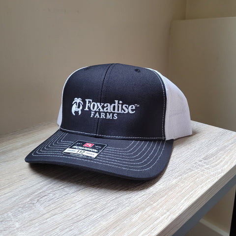 Navy and white cap with 'Foxadise Farms' logo on a wooden surface.