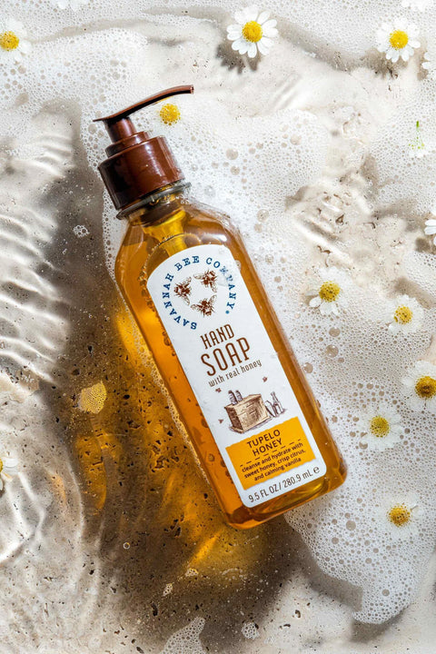 A clear pump bottle of Tupelo Honey Hand Soap with a yellow label, placed on a surface with bubbles and floral patterns.
