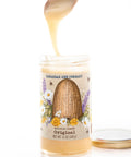Jar of honey from Savannah Bee Company with a spoon pouring honey over it on a white background