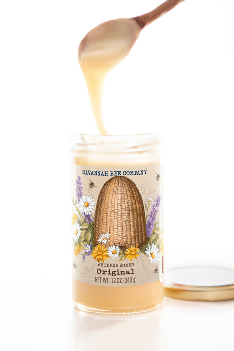 Jar of honey from Savannah Bee Company with a spoon pouring honey over it on a white background