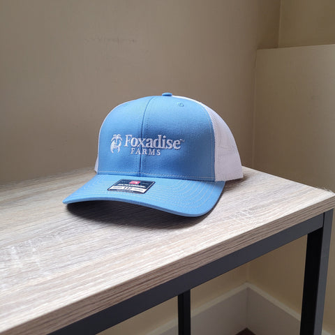 Blue cap with 'Foxadise Farms' logo on a wooden surface