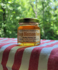 Jar of orange blossom honey from Smiley Honey, LLC on a red and white striped fabric with a green forest background.