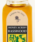 Bottle of Honey Acres Basswood Honey with cork lid on a white background