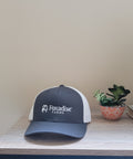 Black and white cap with 'Foxadise Farms' logo on a wooden surface with a plant and books in the background