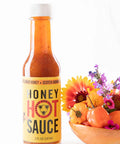 Bottle of honey hot sauce with a bowl of flowers on a white background