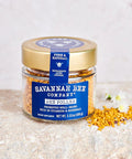 Jar of Savannah Bee Company propolis on a stone surface with flowers.