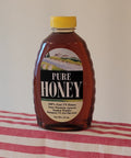 Bottle of pure honey with a yellow cap on a red and white striped tablecloth.