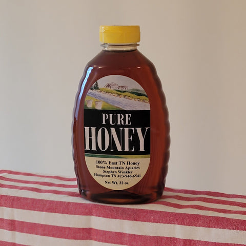 Bottle of pure honey with a yellow cap on a red and white striped tablecloth.