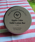 Apple cider solid lotion bar container on a striped fabric background