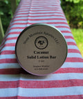 Coconut solid lotion bar from Stone Mountain Apiaries LLC on a red and white striped fabric background.
