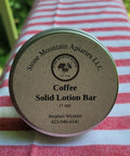 Coffee solid lotion bar container with 'Stone Mountain Apiaries LLC' branding on a striped fabric background.