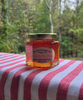 Jar of honey on a red and white striped surface with a forest background