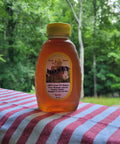 Bottle of honey with a yellow lid on a red and white striped cloth against a green forest background