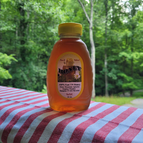 Bottle of honey with a yellow lid on a red and white striped cloth against a green forest background