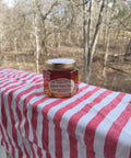 Jar of honey on a red and white striped tablecloth with a forest background