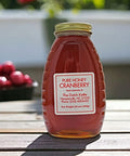 A jar of pure honey labeled Cranberry Honey from The Dutch Kettle, with a background of cranberries.