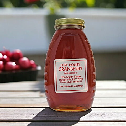 A jar of pure honey labeled Cranberry Honey from The Dutch Kettle, with a background of cranberries.