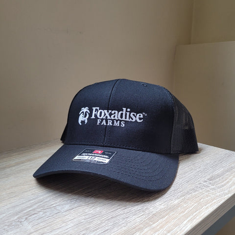 Navy blue cap with 'Foxadise Farms' logo on a wooden surface