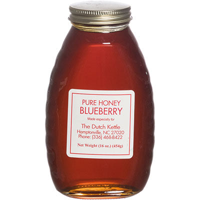 A clear glass jar filled with blueberry honey, with a label that reads 'PURE HONEY BLUEBERRY' along with the brand name and contact information.