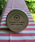 Lavender & Lemon Solid Lotion Bar container on a striped fabric background
