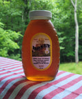 Jar of honey with a label on a red and white striped cloth against a forest background