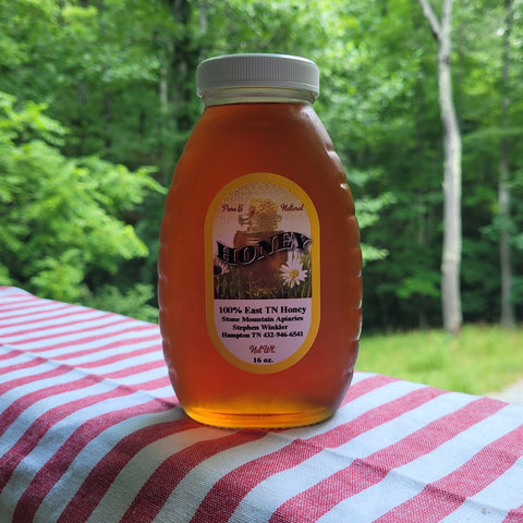 Jar of honey with a label on a red and white striped cloth against a forest background
