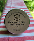 Eucalyptus & Mint Solid Lotion Bar by Stone Mountain Apiaries LLC on a red and white striped fabric background.
