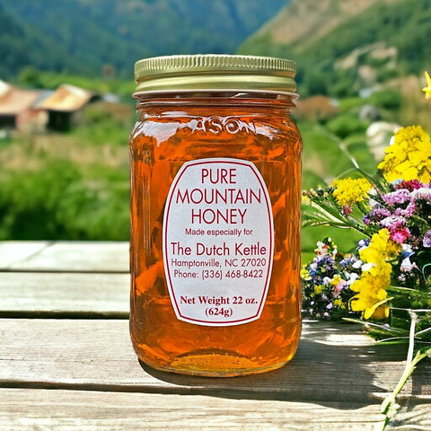 A jar of Pure Mountain Honey with a label that includes the brand name and contact information, placed on a table with a scenic background of mountains and flowers.