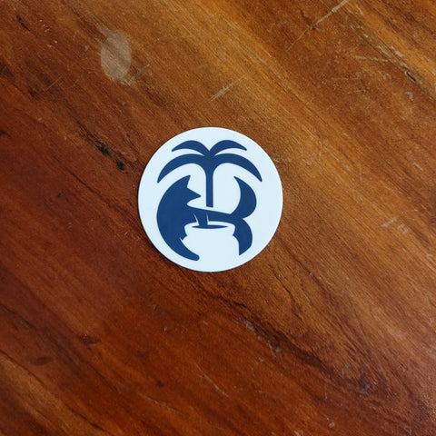 A round vinyl sticker with a blue and white design featuring a palm tree and what appears to be a fox face, placed on a wooden surface.
