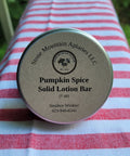 Pumpkin Spice Solid Lotion Bar container on a striped fabric background