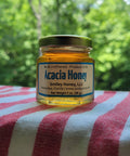 Jar of Acacia honey from Smiley Honey, LLC on a striped fabric with a blurred green background