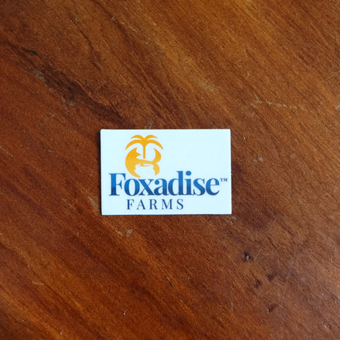 A round vinyl sticker with a blue and white design featuring a palm tree and what appears to be a fox face, placed on a wooden surface.