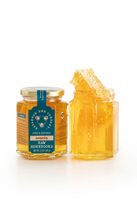 A jar of honey with a piece of honeycomb attached to it, against a white background.