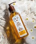 A clear pump bottle of Tupelo Honey Hand Soap with a yellow label, placed on a surface with bubbles and floral patterns.